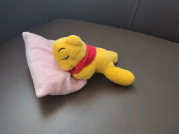 Mini peluche ourson qui dort type Winnie sur oreiller rose