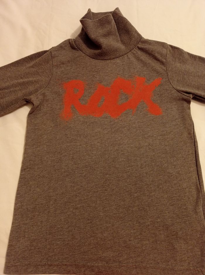 Pull col roulé gris avec inscription devant un roc marquis en rouge