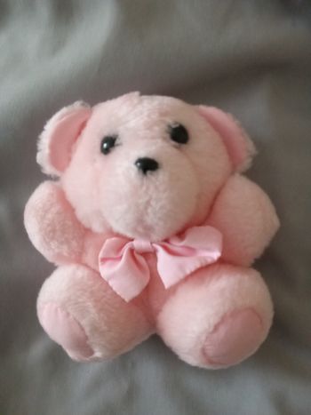 doudou peluche petit ourson ours rose PAMPERS rose clair assis haut 14 cm +/- yeux noirs durs plastique ainsi que son nez posture assis noeud tissu rose niveau du cou