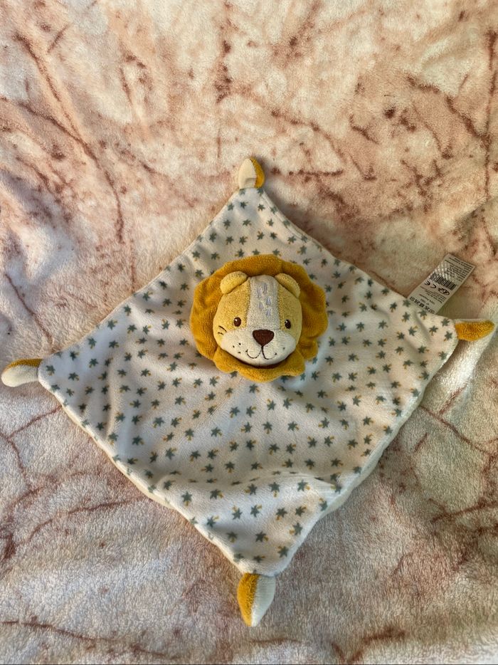 Doudou plat lion jaune/orange  Des motifs des palmier vert  Au dos unis beige  +/- 24cm B&M Occasion en très bon état  Vous achetez le doudou que vous voyez sur la photo