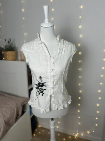 haut chemisier blanc sans manches à volants et broderie florale noire
