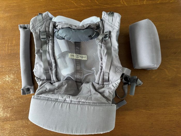 La différence principale est que le PhysioCarrier 2 est une solution tout-en-un (sans accessoire) avec une assise ajustable en largeur pour l’écart du bassin du nourrisson et une partie centrale ajustable en hauteur pour la taille de l’enfant (comme sur l