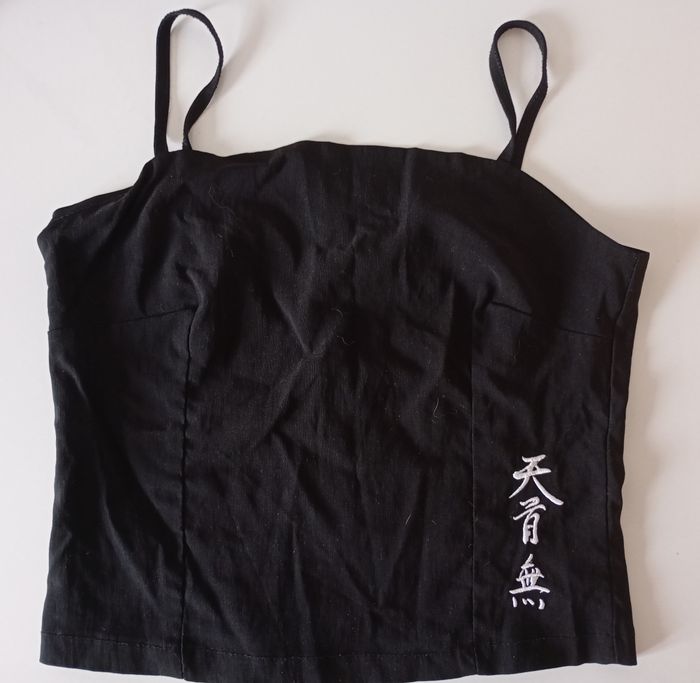 Débardeur noir avec des  bretelles. Taille S . Fermeture éclair. Signes chinois blancs . Viscose polyamide et élasthanne. Très bon état