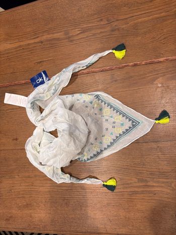 foulard enfant neuf avec étiquette de la marque OKAIDI, orné de pompons jaunes et bleus.