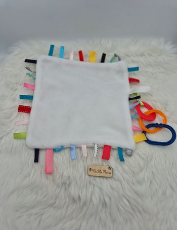 Doudou plat carré blanc étiquettes multicolores anneaux Oxybul