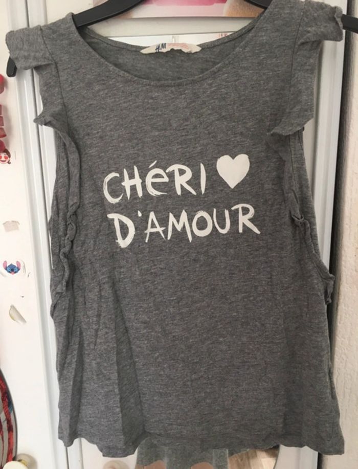 t-shirt gris chiné avec inscription blanche. Sur les manches il y a des volants H&M 12/14 ans