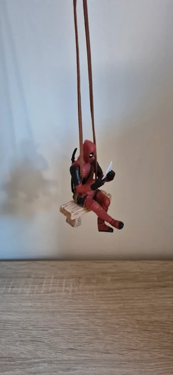 Figurine DeadPool suspendu assis sur un banc.