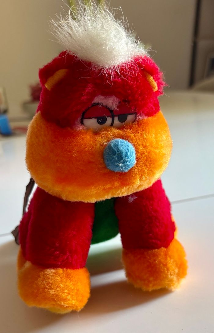 Peluche atypique assise colorée au regard nonchalant