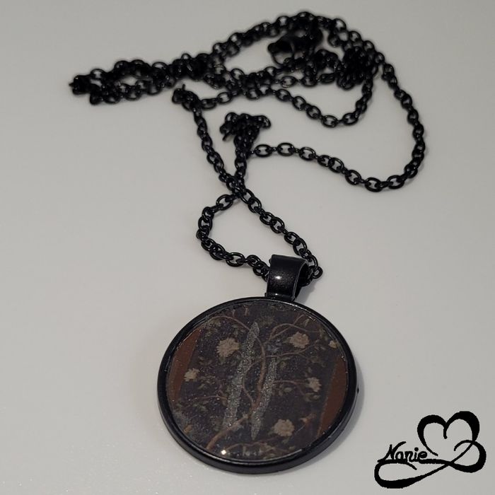 Sautoir, en acier inoxydable et en resine, noir avec des branches et des fleurs.